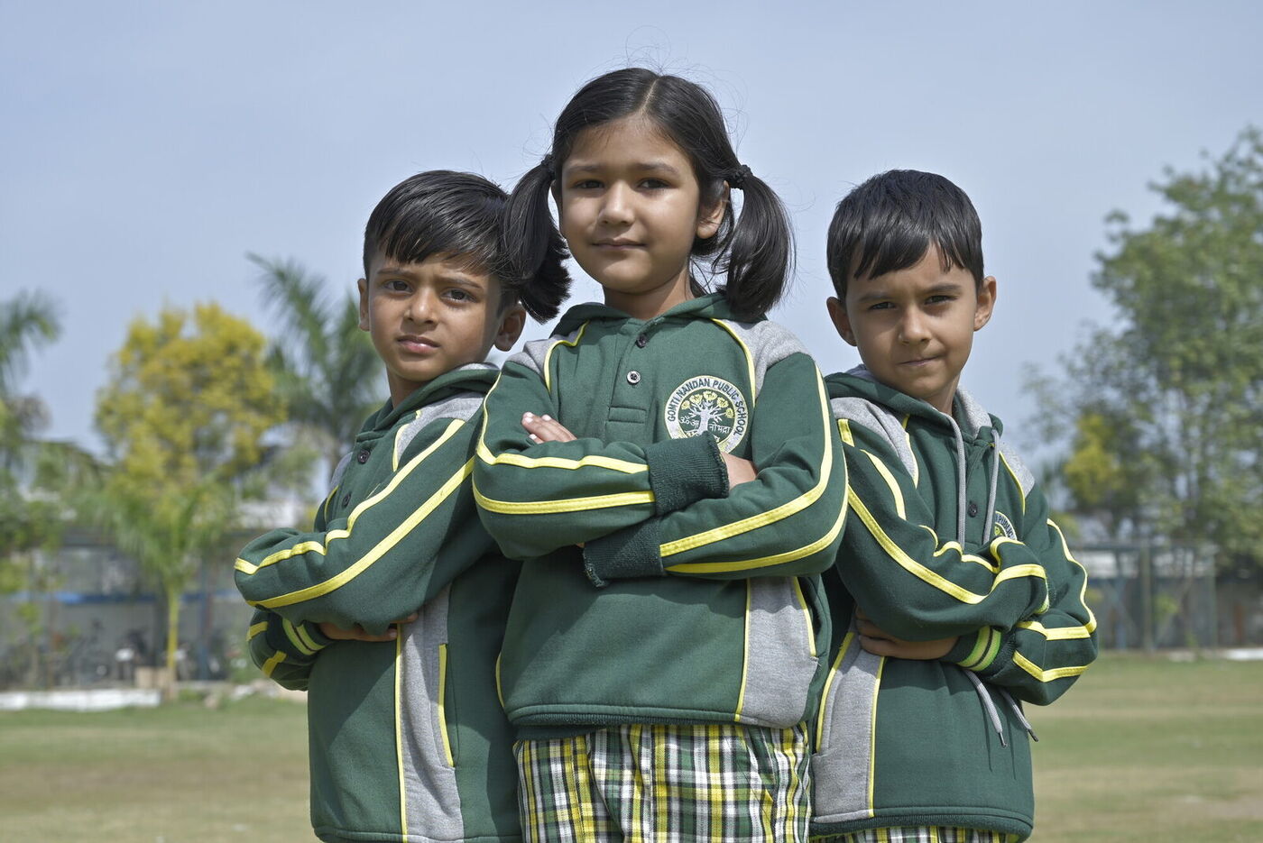Three young students in GNPS winter uniform pose together on the school lawn