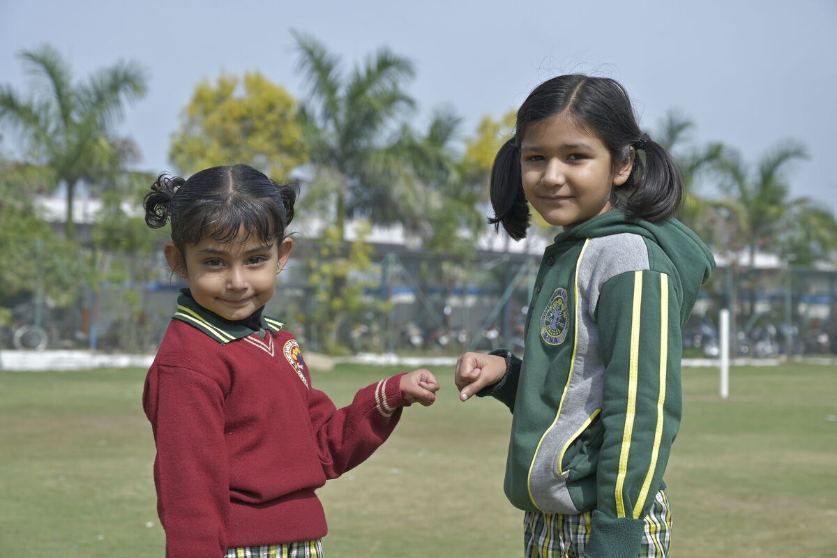 Two young friends share a fist bump on the school lawn