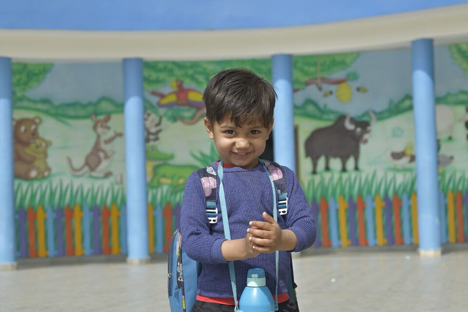 A pre-primary child with his school bag in the kindergarten courtyard